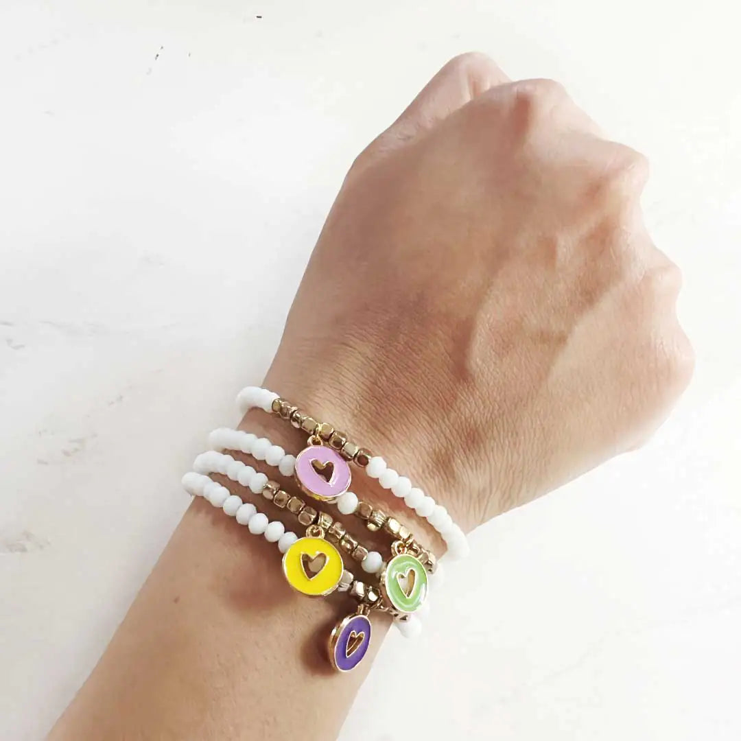 Four colorful charm bracelets stacked on a wrist, featuring heart charms and white beaded design.