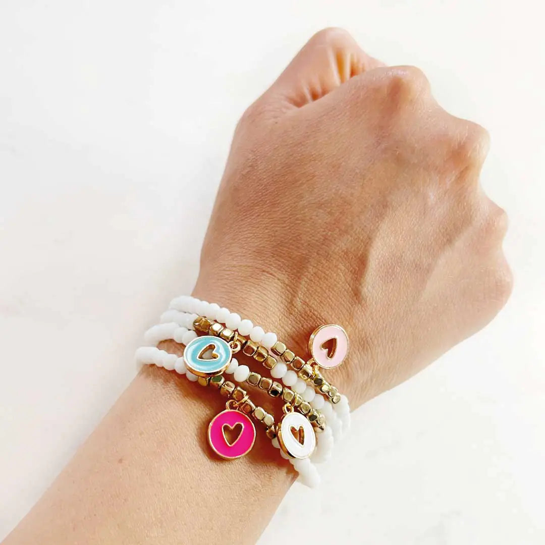 The Lover Bracelet stack featuring 4 hand-beaded charms with heart designs in pink, blue, and white, worn on a wrist.